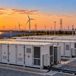 Advait Energy Transitions: battery storage containers with solar panels, wind turbines and transmission towers at sunset