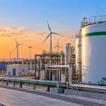 Green Hydrogen Offtake Commitments: storage tanks and pipework at a green hydrogen plant with solar panels and wind turbines at sunset