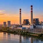 Buxar Thermal: a coal-fired power plant with chimneys and cooling towers beside a river at sunset