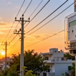 Smart Meter Revenue: a smart electricity meter on a wall with power lines and homes behind it at sunset