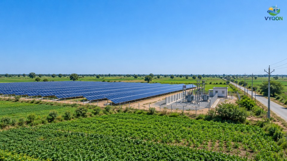 Solar panel rows on green farmland beside a small substation and a line of electricity poles